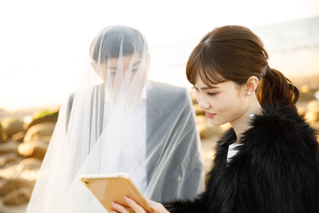 奈多海岸にてFLVSで映し出される写真を確認する洋装の新郎新婦