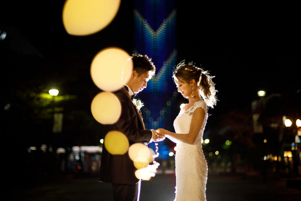 洋装の婚礼前撮りで、夜の福岡タワーをバックにLEDが新郎新婦に向かっていくイルミネーション夜景撮影