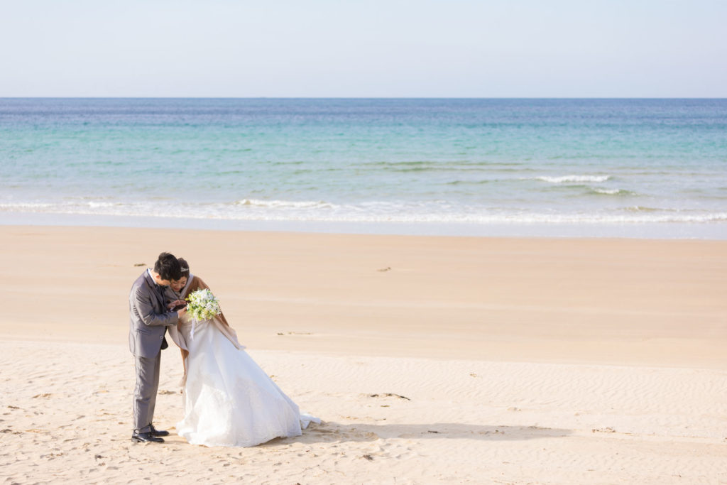 海を背景にFLVSのタブレットで写りを確認する新郎新婦様